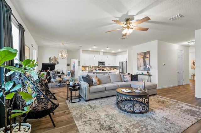 living area with baseboards, visible vents, wood finished floors, and ceiling fan with notable chandelier