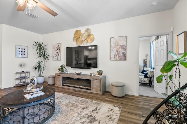living area featuring visible vents, wood finished floors, baseboards, and ceiling fan