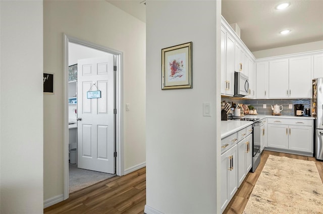 kitchen featuring white cabinets, decorative backsplash, stainless steel appliances, and wood finished floors