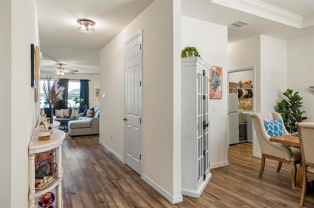 corridor featuring baseboards, ornamental molding, visible vents, and wood finished floors