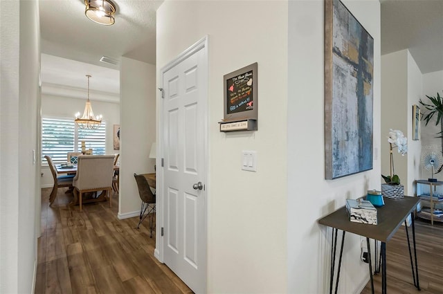 hall featuring an inviting chandelier, visible vents, baseboards, and dark wood-style floors