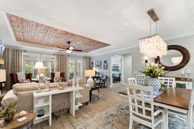 living room with a tray ceiling, light wood-style flooring, ornamental molding, baseboards, and a chandelier