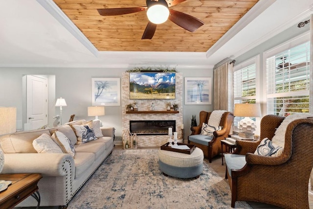 living room featuring wood ceiling, a raised ceiling, a stone fireplace, ceiling fan, and ornamental molding