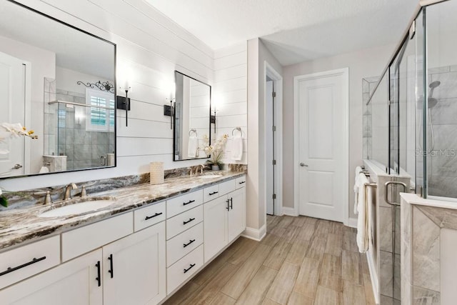 bathroom featuring a shower stall, double vanity, wood finished floors, and baseboards