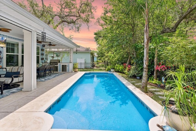 pool at dusk featuring a ceiling fan, fence, exterior kitchen, and a patio area