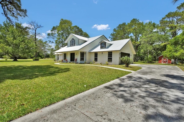 view of front facade with covered porch, driveway, a garage, metal roof, and a front lawn