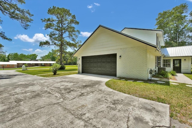 view of side of home featuring a lawn, brick siding, metal roof, a garage, and concrete driveway