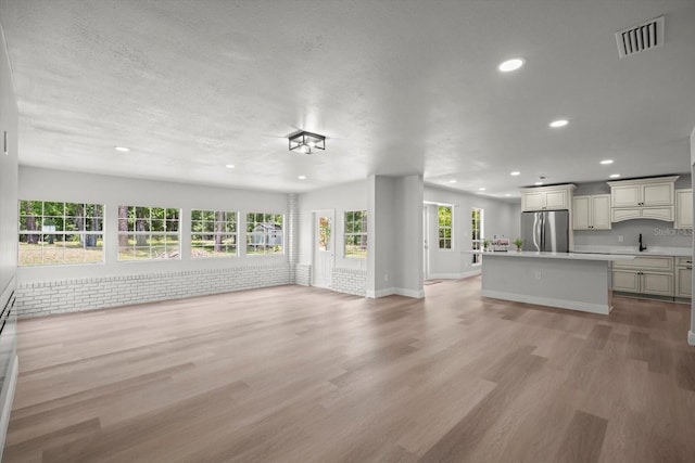 unfurnished living room featuring a sink, visible vents, recessed lighting, light wood finished floors, and baseboards