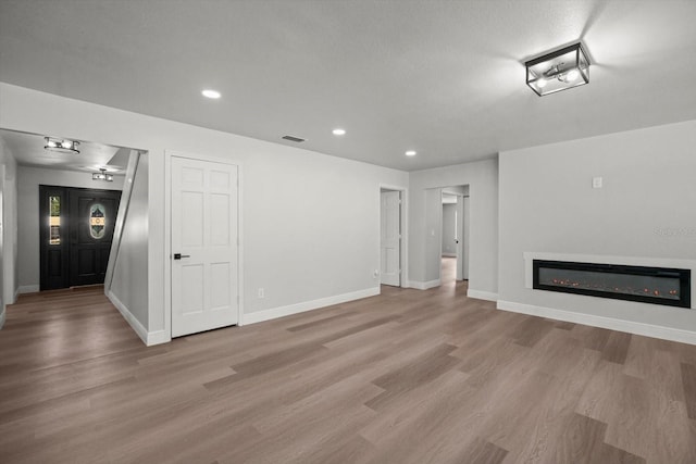 unfurnished living room featuring a glass covered fireplace, baseboards, and light wood-style flooring