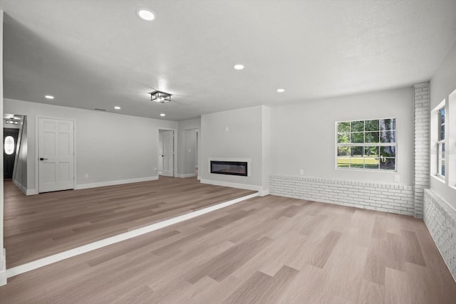unfurnished living room featuring recessed lighting, light wood-type flooring, baseboards, and a glass covered fireplace