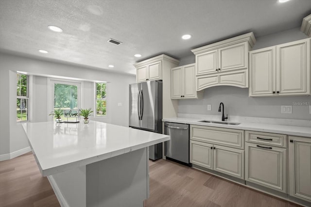 kitchen with a sink, stainless steel appliances, a textured ceiling, light wood-type flooring, and recessed lighting