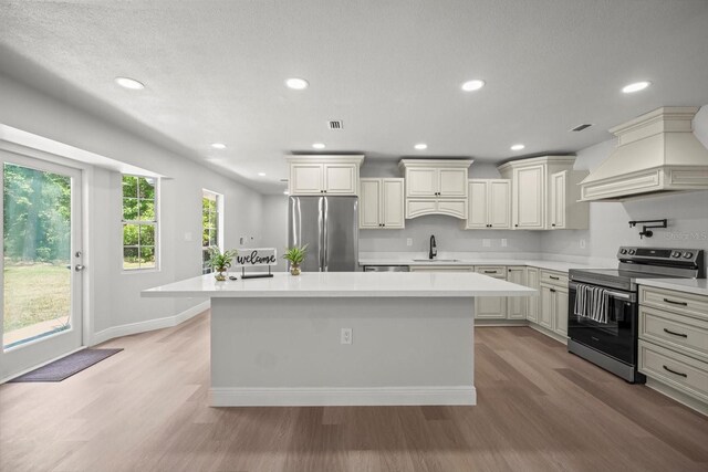 kitchen featuring a center island, light wood-style flooring, stainless steel appliances, light countertops, and custom range hood