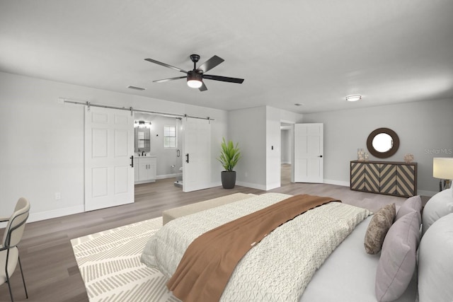 bedroom with a ceiling fan, a barn door, baseboards, visible vents, and wood finished floors