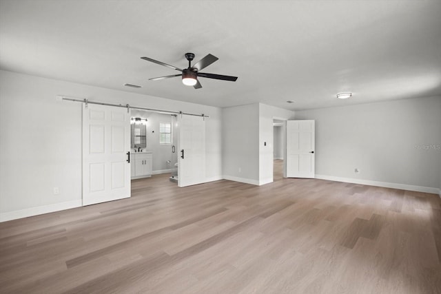 unfurnished bedroom featuring a barn door, baseboards, visible vents, and light wood-style floors