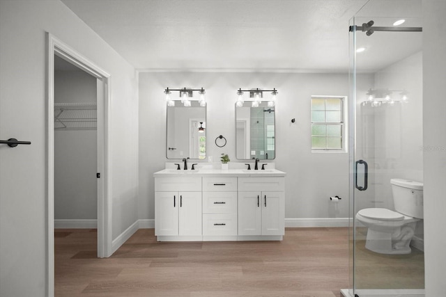 bathroom with a sink, toilet, wood finished floors, double vanity, and baseboards