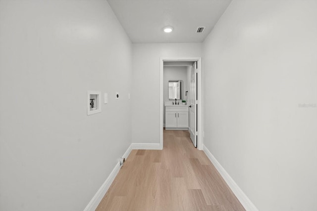 corridor featuring baseboards, light wood-style flooring, visible vents, and a sink