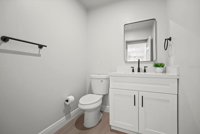 half bath with toilet, baseboards, vanity, and wood finished floors
