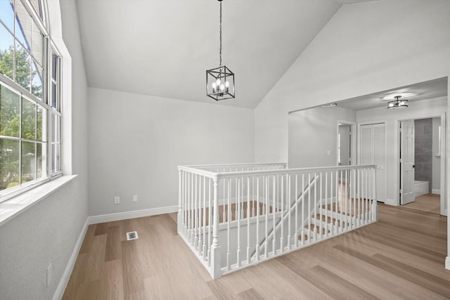 hallway featuring a healthy amount of sunlight, an upstairs landing, an inviting chandelier, and wood finished floors