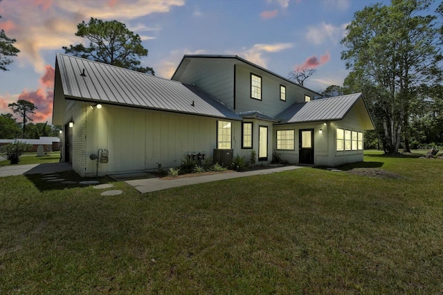 back of house with metal roof, board and batten siding, and a lawn