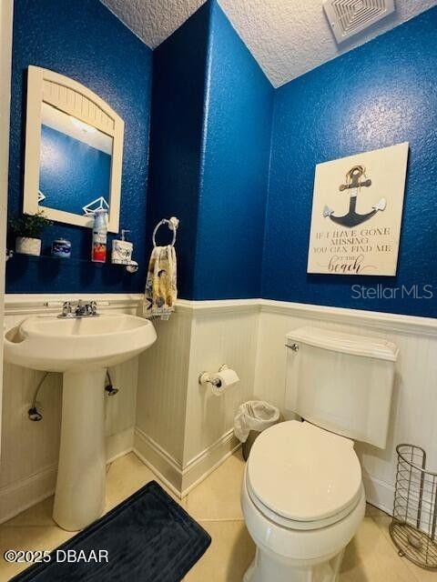 3000 Ocean Shore Blvd Unit 150, Ormond Beach, FL 32176 - bathroom featuring toilet, a wainscoted wall, tile patterned floors, and a textured ceiling