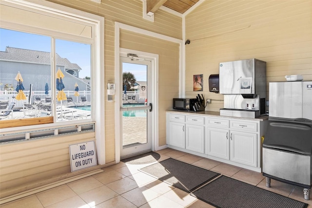 50 Nantucket Dr, Palm Coast, FL 32137 - kitchen with light tile patterned floors, white cabinets, wooden walls, black microwave, and high vaulted ceiling