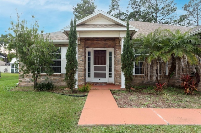 view of front facade with a front yard, roof with shingles, and brick siding