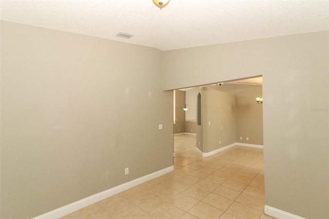 empty room with a textured ceiling, visible vents, arched walkways, light tile patterned floors, and baseboards