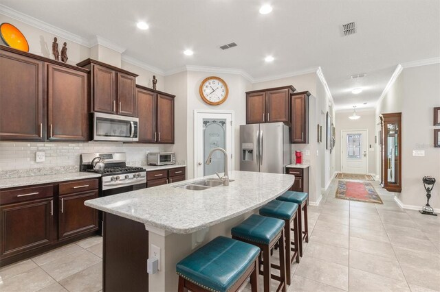 kitchen with appliances with stainless steel finishes, a sink, light tile patterned floors, crown molding, and a kitchen island with sink