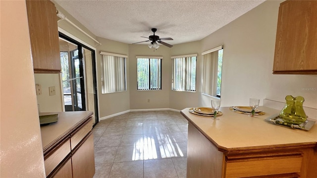 unfurnished dining area featuring plenty of natural light, light tile patterned floors, a ceiling fan, a textured ceiling, and baseboards