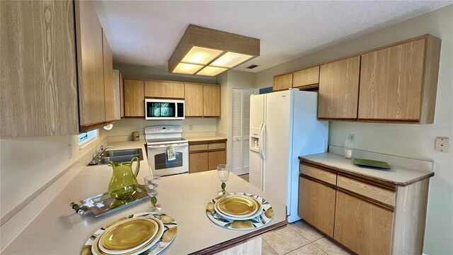 kitchen featuring white appliances, a sink, light countertops, and light tile patterned floors