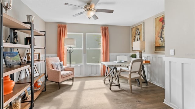 sitting room with a ceiling fan, a wainscoted wall, and wood finished floors