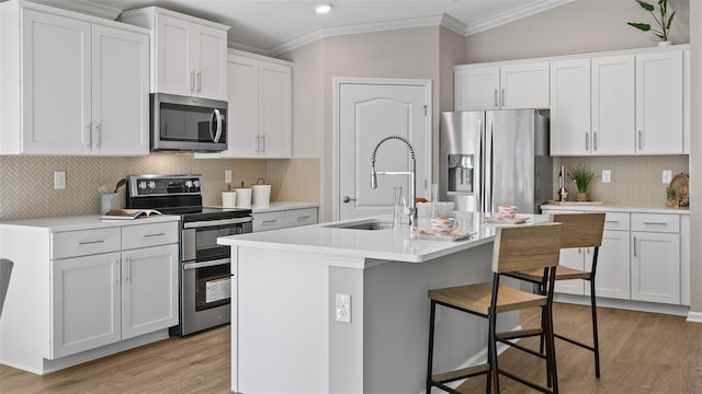 kitchen with light wood-style floors, ornamental molding, a breakfast bar, and appliances with stainless steel finishes