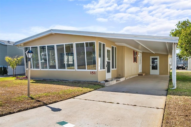 151 Lookout Dr, Flagler Beach, FL 32136 - manufactured / mobile home featuring an attached carport, driveway, a front lawn, and a sunroom