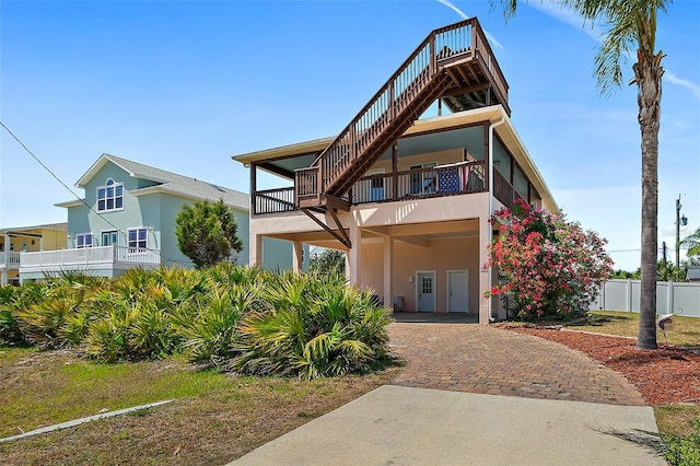 coastal home with a carport, a balcony, fence, stucco siding, and decorative driveway
