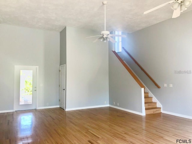unfurnished living room with a ceiling fan, healthy amount of natural light, wood finished floors, baseboards, and a towering ceiling