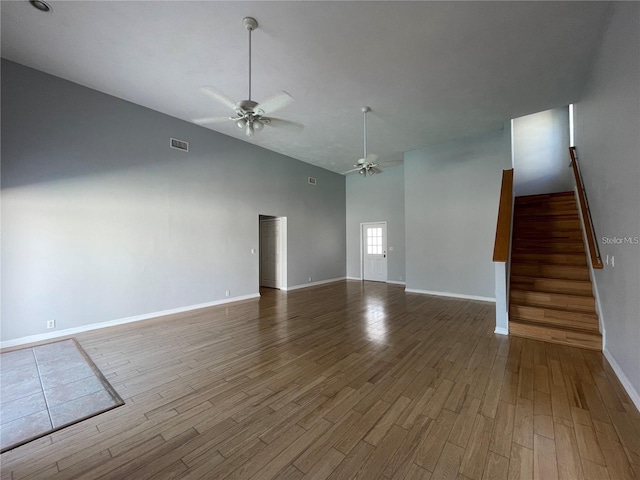 unfurnished living room with ceiling fan, stairway, wood finished floors, high vaulted ceiling, and baseboards