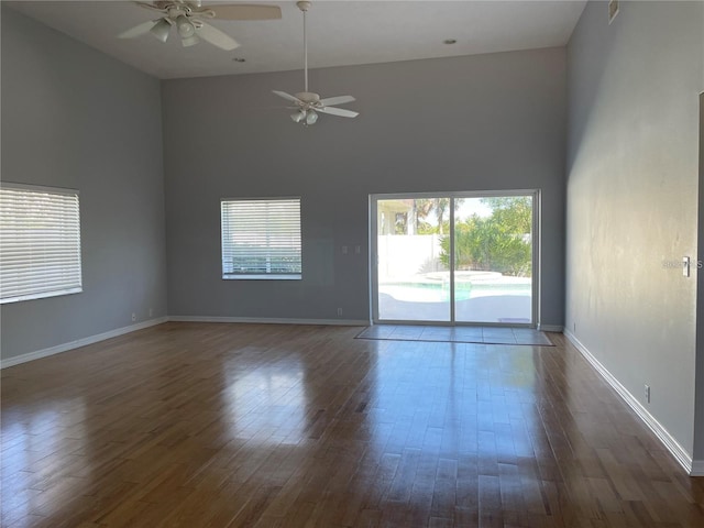 empty room with a ceiling fan, a towering ceiling, dark wood-style flooring, and baseboards