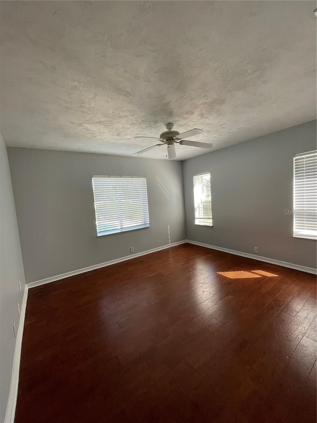 empty room with baseboards, dark wood-style floors, a textured ceiling, and a ceiling fan