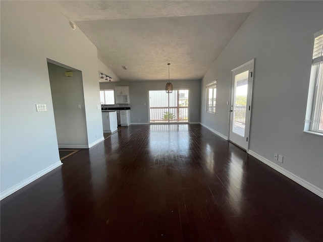 unfurnished living room featuring dark wood-style floors, vaulted ceiling, baseboards, and a chandelier