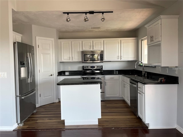 kitchen with appliances with stainless steel finishes, a sink, dark countertops, and white cabinetry