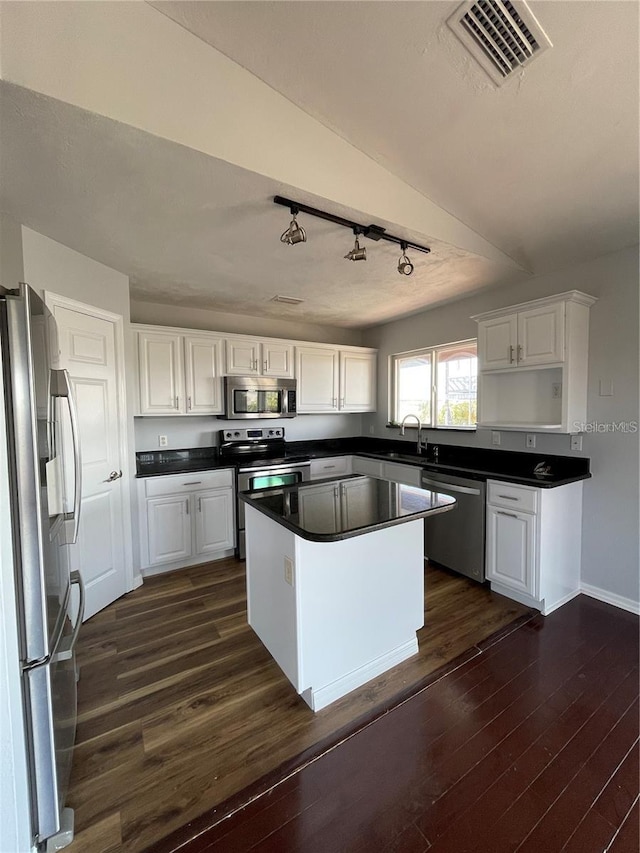 kitchen featuring stainless steel appliances, a sink, white cabinetry, dark wood-style flooring, and dark countertops