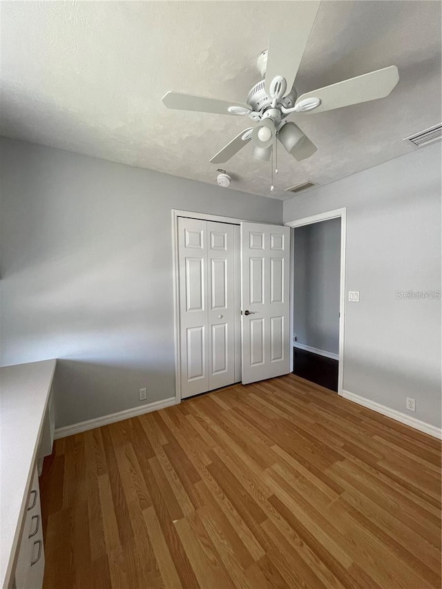 unfurnished bedroom featuring baseboards, wood finished floors, a closet, and ceiling fan