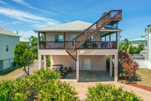 back of property with stucco siding, a carport, fence, driveway, and stairs