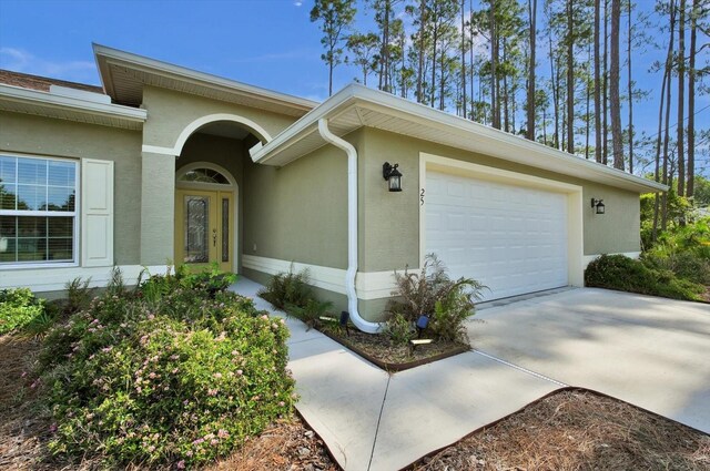 entrance to property featuring stucco siding, a garage, and driveway
