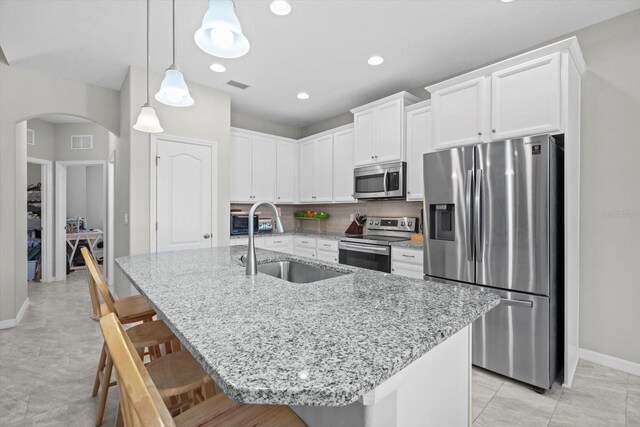 kitchen with appliances with stainless steel finishes, a sink, arched walkways, a kitchen bar, and baseboards