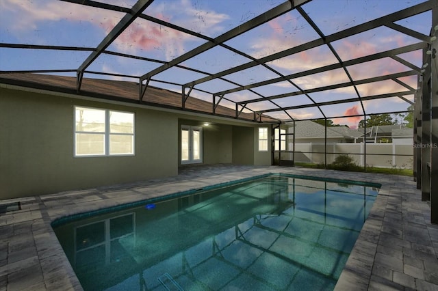 pool at dusk with a patio, french doors, and a lanai