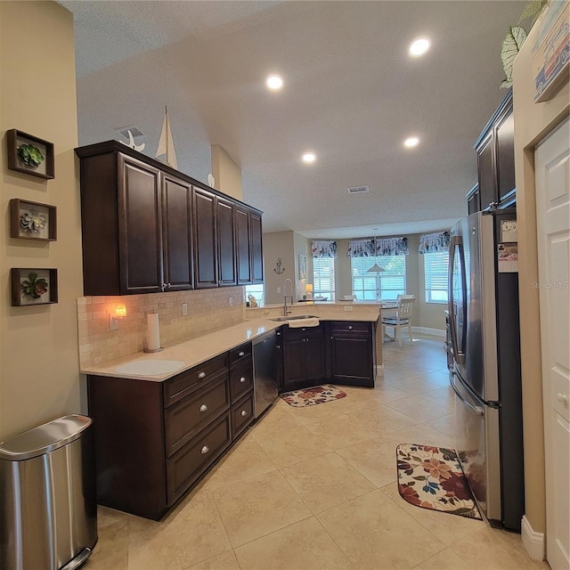 kitchen featuring appliances with stainless steel finishes, a peninsula, a sink, light countertops, and dark brown cabinetry