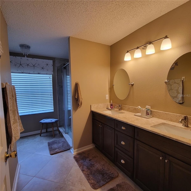 bathroom featuring a textured ceiling, double vanity, tile patterned flooring, a shower stall, and baseboards