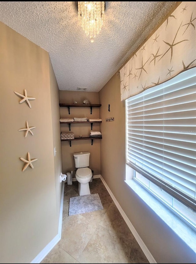 bathroom featuring a textured ceiling, toilet, baseboards, and tile patterned flooring