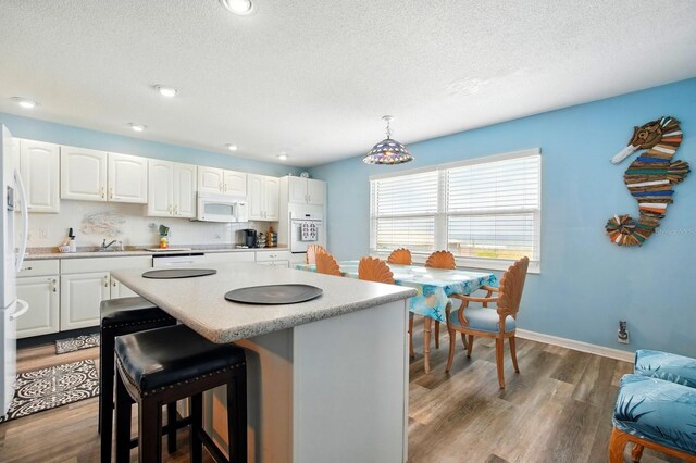 7029 N Ocean Shore Blvd, Palm Coast, FL 32137 - kitchen featuring a textured ceiling, a center island, white appliances, a kitchen breakfast bar, and white cabinets
